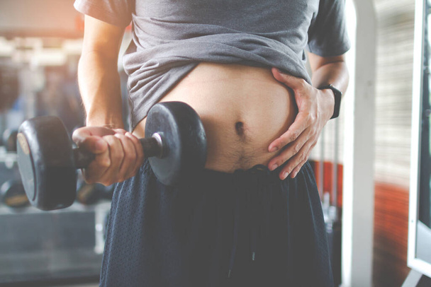 Overweight fatty belly of man and holding a dumbbell. Man diet lifestyle concept to reduce belly and shape up healthy stomach muscle. Man fat. - 写真・画像