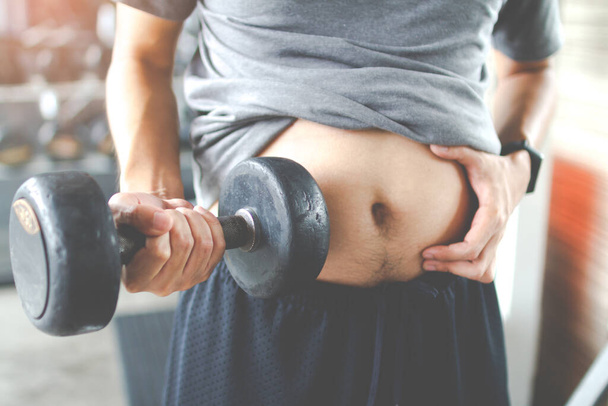 Overweight fatty belly of man and holding a dumbbell. Man diet lifestyle concept to reduce belly and shape up healthy stomach muscle. Man fat. - 写真・画像