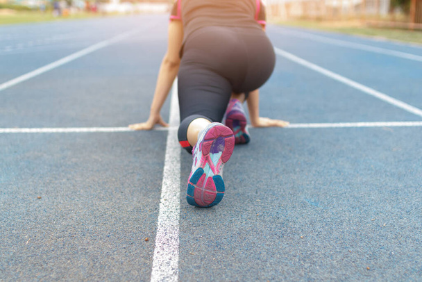 woman in running start pose on the blue running track in stadium - Фото, зображення