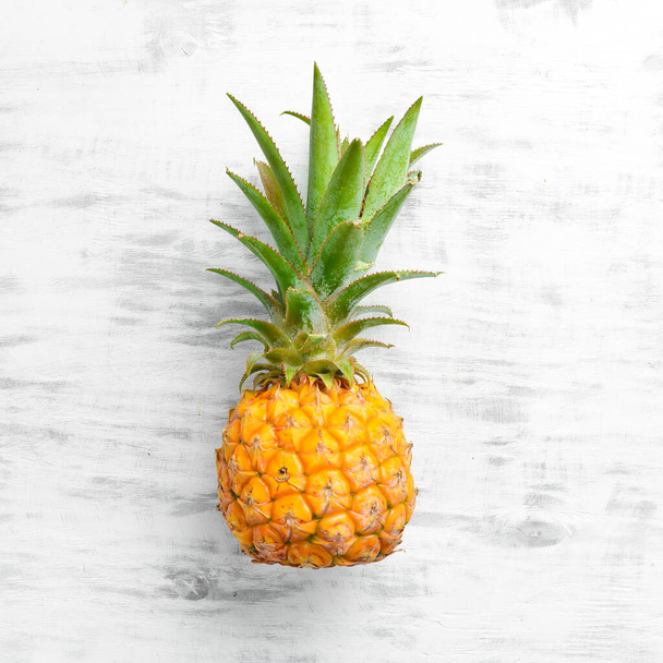 Pineapple white background. Ripe baby pineapple on a white wooden background. Tropical fruits. Top view. Free space for text. - 写真・画像