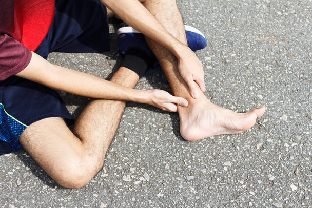 Hombre deportivo sosteniendo el tobillo con dolor debido a un esguince de tobillo. Lesión por concepto de entrenamiento - Foto, Imagen