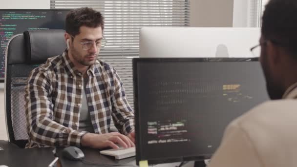 オフィスで新しいソフトウェアを開発するPCコンピュータ上のプログラムコードを書く2つの多民族IT専門家のスタブショット - 映像、動画