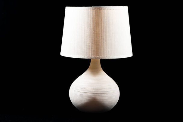 Una lámpara de noche clásica de color blanco, beige o crema sobre un fondo negro con un dibujo de sombra estética en frente - Foto, Imagen
