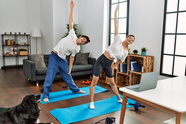 Young caucasian couple smiling happy training yoga with dog at home. - Foto, Imagem