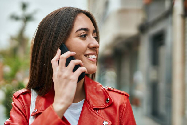 Young hispanic woman smiling happy talking on the smartphone at the city. - 写真・画像