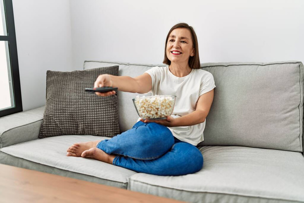 Hispanische Frau mittleren Alters schaut sich einen Film an, der zu Hause Popcorn isst - Foto, Bild