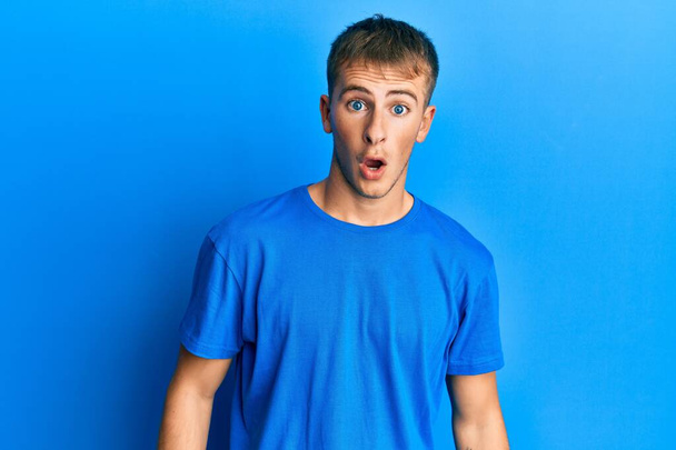Young caucasian man wearing casual blue t shirt afraid and shocked with surprise and amazed expression, fear and excited face.  - Фото, изображение
