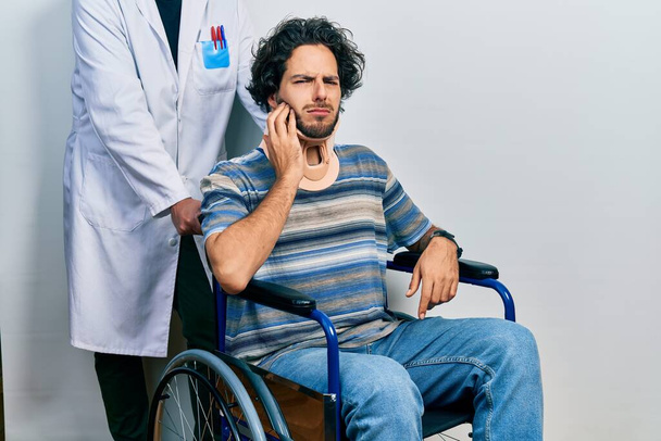 Handsome hispanic man sitting on wheelchair wearing neck collar touching mouth with hand with painful expression because of toothache or dental illness on teeth. dentist  - Photo, Image