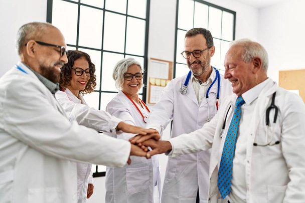 Bir grup orta yaşlı doktor klinikteki tıbbi toplantıda el ele tutuşup mutlu bir şekilde gülümsüyor.. - Fotoğraf, Görsel