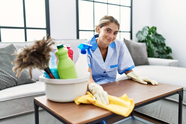 Young caucasian woman wearing cleaner uniform cleaning table at home - Photo, Image