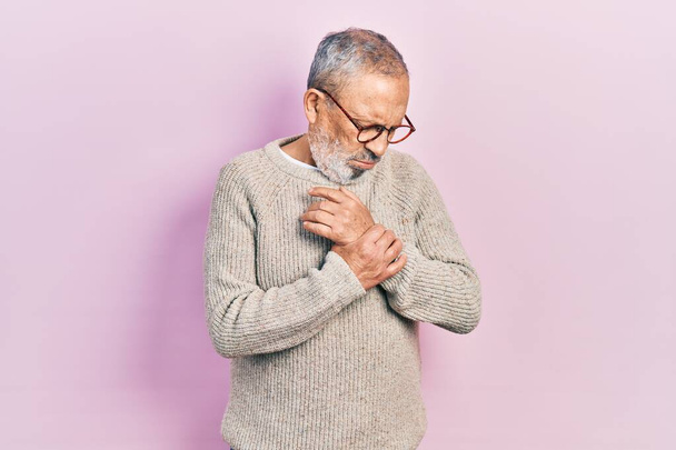 Handsome senior man with beard wearing casual sweater and glasses suffering pain on hands and fingers, arthritis inflammation  - Fotoğraf, Görsel
