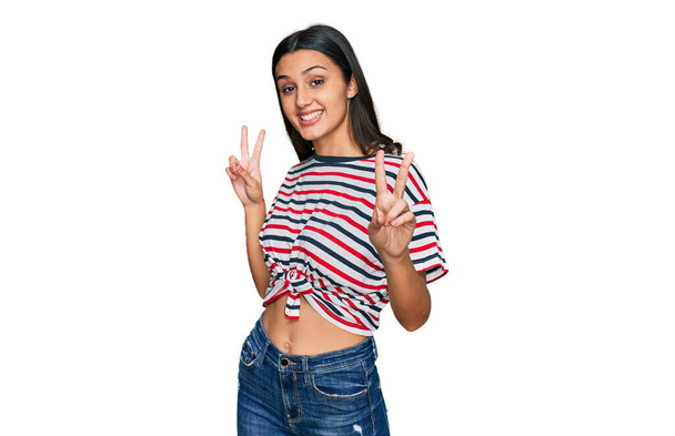 Young hispanic girl wearing casual clothes smiling looking to the camera showing fingers doing victory sign. number two.  - Foto, immagini