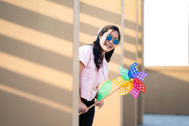 Aasialainen nainen virkaa ja pelata Tuulimylly Lelu värikäs sateenkaaren väri rakennuksen katolla auringonlaskun aikaan. - Valokuva, kuva