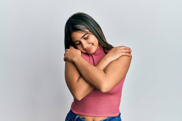 Junge lateinamerikanische Frau in lässiger Kleidung, die sich glücklich und positiv umarmt und selbstbewusst lächelt. Selbstliebe und Selbstfürsorge  - Foto, Bild