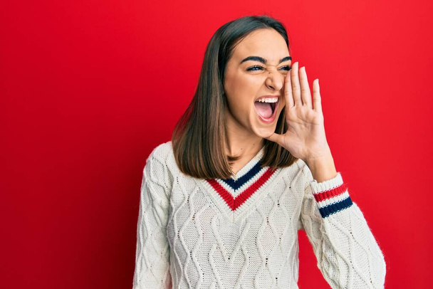 Young brunette girl wearing casual student sweater shouting and screaming loud to side with hand on mouth. communication concept.  - Photo, Image