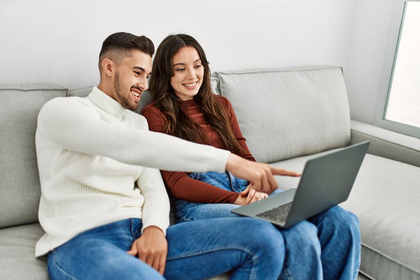Giovane coppia ispanica utilizzando il computer portatile seduto sul divano a casa. - Foto, immagini