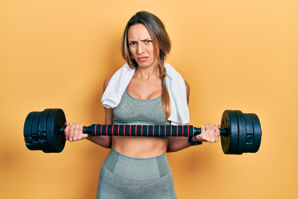 Beautiful hispanic woman wearing sportswear using dumbbells clueless and confused expression. doubt concept.  - Foto, immagini