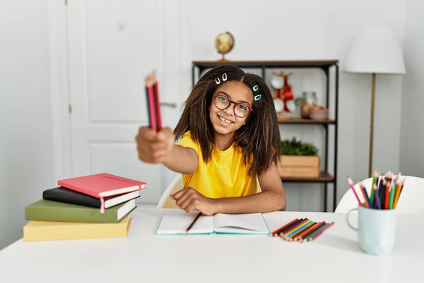 African american girl doing school homework holding pencils at home - Foto, Imagen