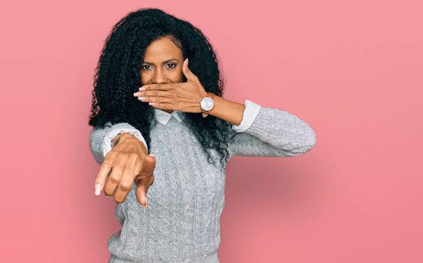 Μεσαίωνας Αφροαμερικανή γυναίκα που φοράει καθημερινά ρούχα γελώντας μαζί σου, δείχνοντας με το δάχτυλο την κάμερα με το χέρι πάνω από το στόμα, έκφραση ντροπής  - Φωτογραφία, εικόνα