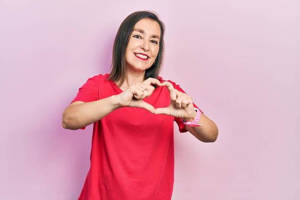 Middle age hispanic woman wearing casual clothes smiling in love doing heart symbol shape with hands. romantic concept.  - Фото, изображение