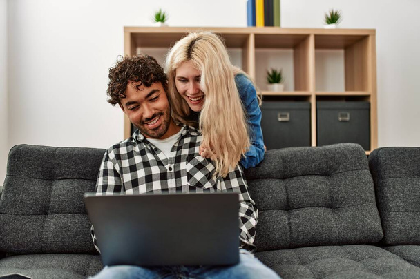 Giovane coppia utilizzando il computer portatile seduto sul divano a casa. - Foto, immagini