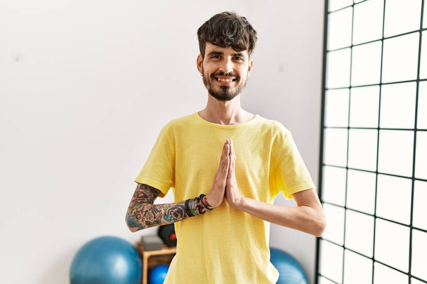 Young hispanic man smiling confident training yoga at center. - 写真・画像