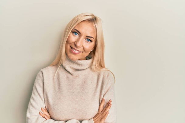 Jonge blonde vrouw draagt casual winter coltrui vrolijk gezicht glimlachend met gekruiste armen kijkend naar de camera. positieve persoon.  - Foto, afbeelding