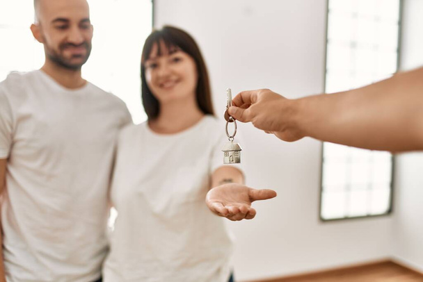 Młoda latynoska para uśmiecha się szczęśliwa i przytula trzymając klucz nowego domu. - Zdjęcie, obraz