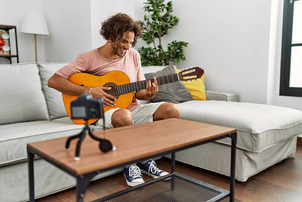 Jeune homme hispanique enregistrement avec caméra jouant de la guitare classique à la maison. - Photo, image