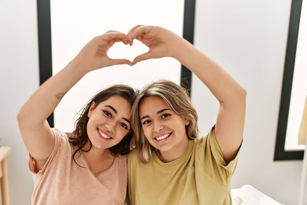 Young couple smiling happy doing heart symbol with hands at bedroom. - Photo, Image