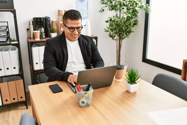 Молодий латинський бізнесмен посміхається щаслива робота з ноутбуком в офісі
. - Фото, зображення