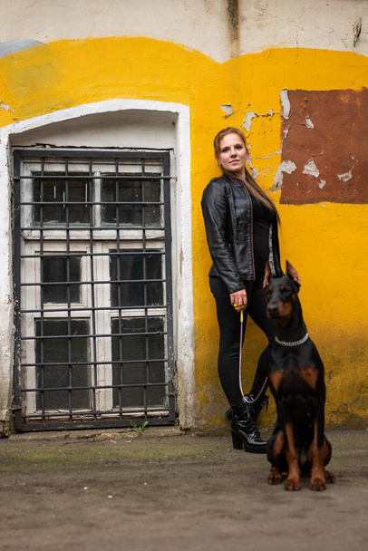 Une fille en cuir, avec un Doberman, dans une vieille cour. - Photo, image
