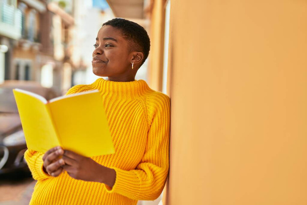 Giovane donna afroamericana sorridente libro di lettura felice in città. - Foto, immagini
