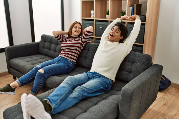Junges Paar lächelt glücklich entspannt auf dem heimischen Sofa sitzend. - Foto, Bild