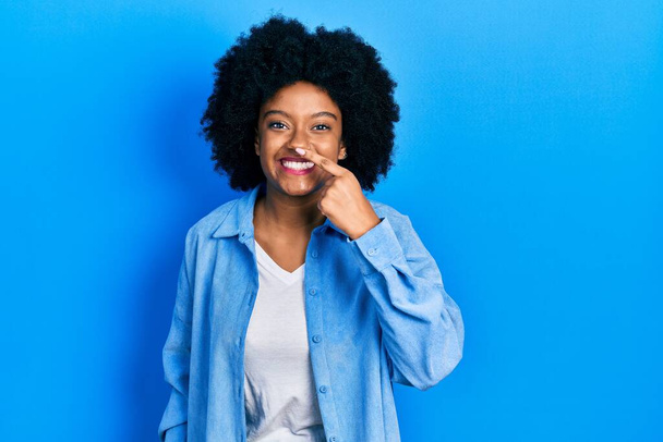 Молодая африканская американка в повседневной одежде, указывая пальцем на лицо и нос, весело улыбается. концепция красоты  - Фото, изображение