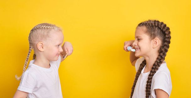 cheerful girls brushing teeth on yellow background, toddler and teen girls, electric or bamboo brush concept, toothbrushes for kids - Фото, зображення