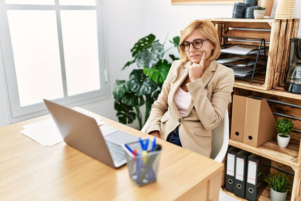 Moyen âge femme blonde travaillant avec une expression sérieuse au bureau - Photo, image