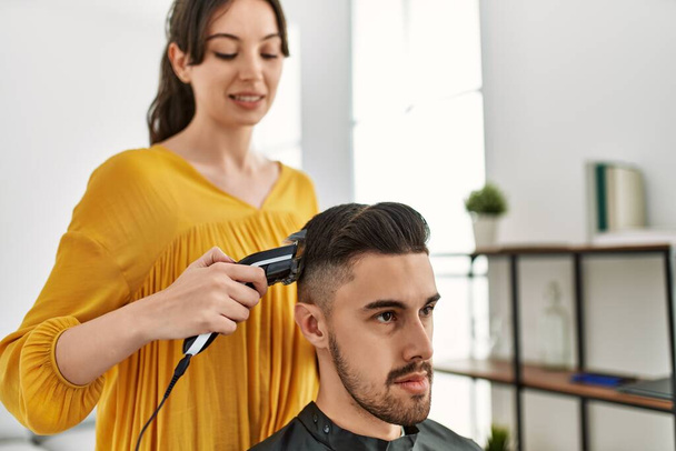 Nuori latino kampaaja nainen leikkaus miehen hiukset käyttäen sähköinen partaveitsi kone kauneuskeskus. - Valokuva, kuva