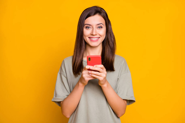 Photo of young beautiful happy positive cheerful smiling girl typing in smartphone isolated on yellow color background. - Foto, Bild