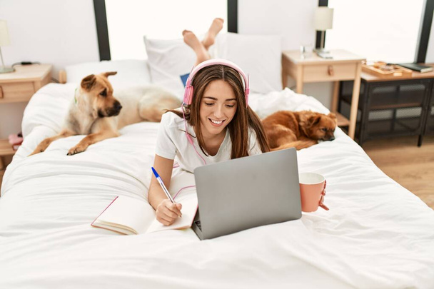 Giovane donna ispanica che studia sdraiato sul letto con i cani in camera da letto - Foto, immagini