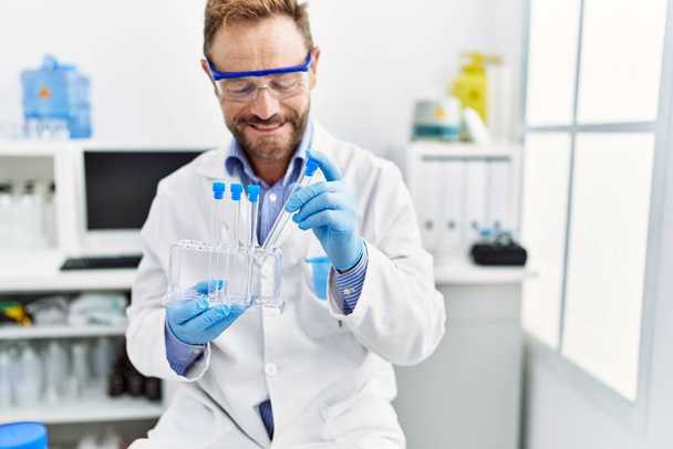 Hombre hispano de mediana edad vistiendo uniforme científico trabajando en laboratorio - Foto, Imagen