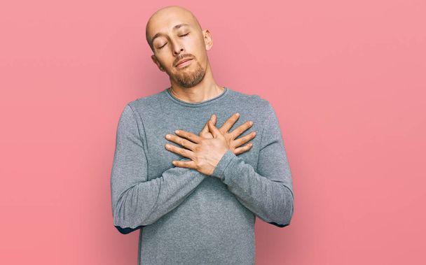 Bald man with beard wearing casual clothes smiling with hands on chest with closed eyes and grateful gesture on face. health concept.  - Zdjęcie, obraz