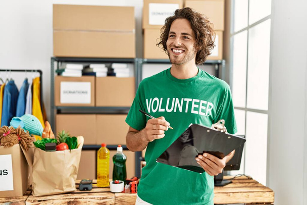 Fiatal spanyol önkéntes férfi mosolyog boldog írás vágólapon jótékonysági központ. - Fotó, kép