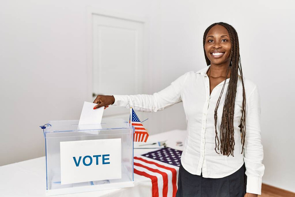 Young african american voter woman putting vote in ballot box at electoral college. - Photo, Image
