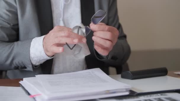 öltönyös férfi letörli a szalvétás szemüveget, miközben irodai dokumentumokat olvas, közelkép - Felvétel, videó