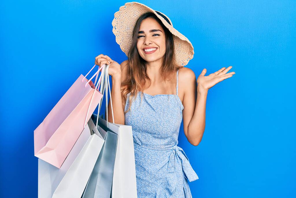 Young hispanic girl holding shopping bags celebrating victory with happy smile and winner expression with raised hands  - Foto, immagini