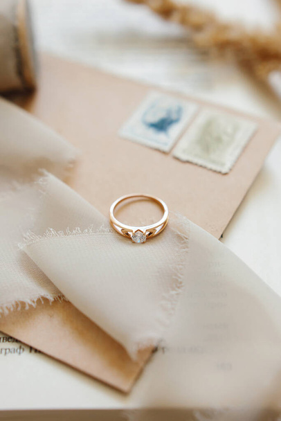 Jewelry, engagement gold ring with sparkling white stone, diamond on a beige background. Selective focus. Vertical photo. - 写真・画像