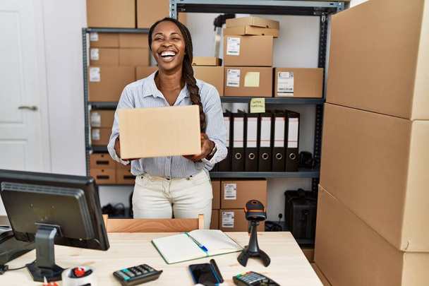 Африканська жінка працює в невеликому бізнесі екомерс тримаючи коробку посміхаючись і сміючись голосно, тому що смішний жарт.  - Фото, зображення