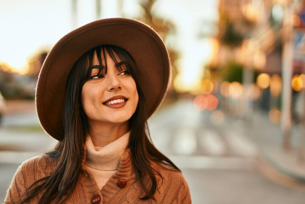 Brunette woman wearing winter hat smiling outdoors at the city on sunset - Foto, immagini