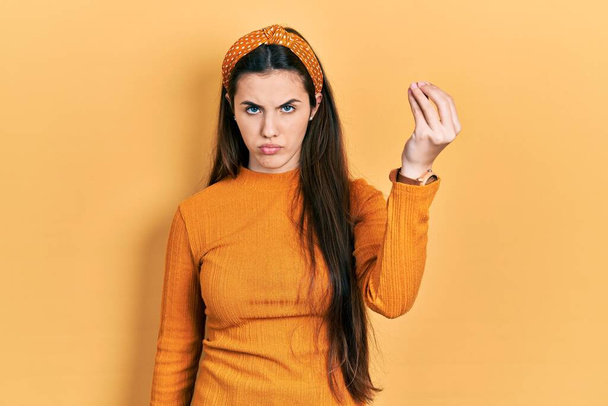 młody brunetka nastolatek noszenie casual żółty sweter robi włoski gest z ręki i palców pewny wyraz twarzy  - Zdjęcie, obraz